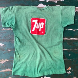 May include: Green short-sleeved t-shirt with a red 7Up logo patch on the back.