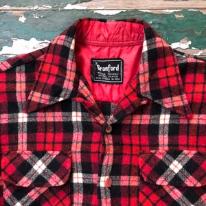 May include: A red, black, and white plaid flannel shirt with a red quilted lining. The shirt has two chest pockets and a button-down front. The label reads "Branford".