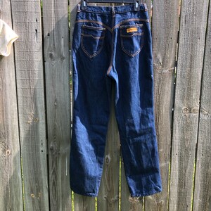 May include: A pair of dark blue denim jeans with a high waist and a straight leg. The jeans have a brown leather patch on the back with the text "Lee" in white.
