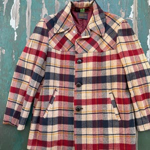 May include: A Pendleton brand jacket featuring a plaid pattern in red, navy blue, tan, and yellow. The jacket has a collared neckline, a front button closure with three dark buttons, and two side pockets. The interior is lined in maroon.