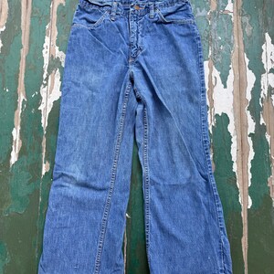 Op de afbeelding: Vintage blauwe denim jeans met een uitlopende pijp. De jeans hebben een klassieke vijf-zakken stijl, een knoop- en ritssluiting en een vervaagde wassing. De naden zijn zichtbaar en de denim vertoont tekenen van slijtage.