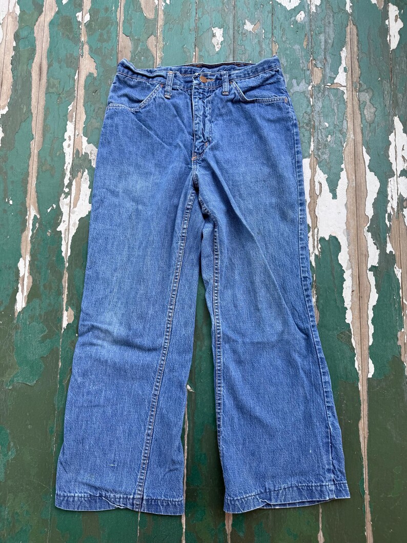 Op de afbeelding: Vintage blauwe denim jeans met een uitlopende pijp. De jeans hebben een klassieke vijf-zakken stijl, een knoop- en ritssluiting en een vervaagde wassing. De naden zijn zichtbaar en de denim vertoont tekenen van slijtage.