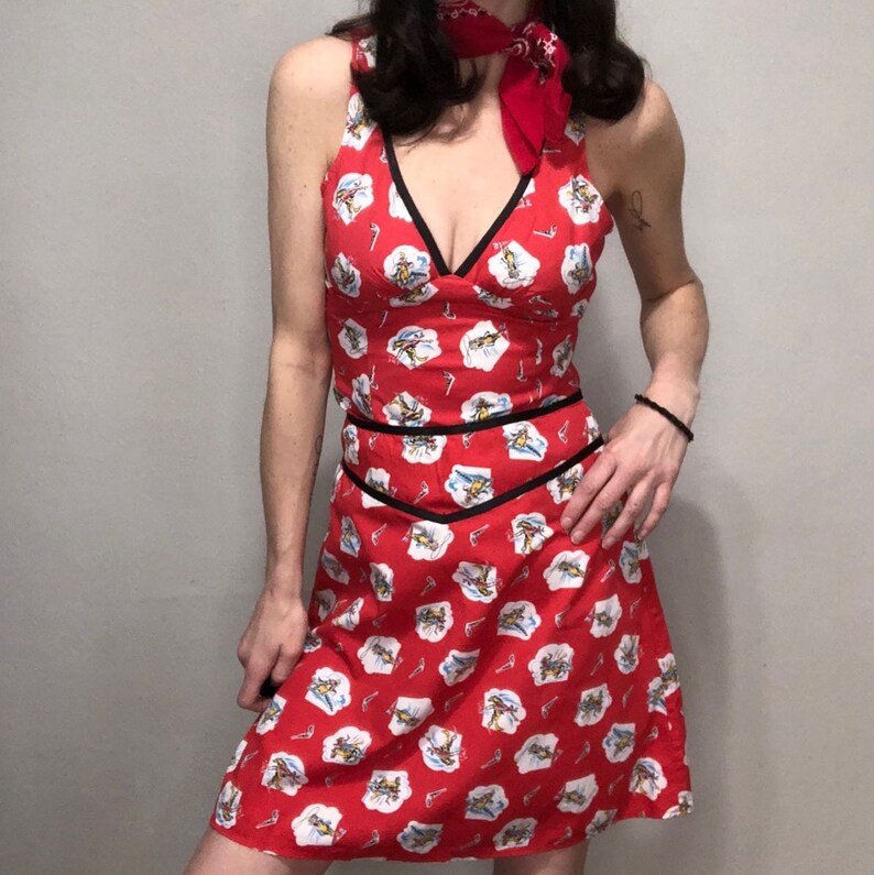 Peut inclure: Une robe rouge sans manches avec une bordure noire et un imprim&eacute; blanc de skieurs. La robe a un d&eacute;collet&eacute; en V profond et un corsage ajust&eacute;.