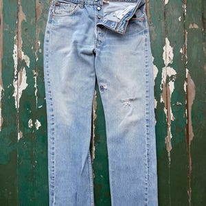 May include: A white ceramic mug with a black handle and the text "But First, Coffee" in a bold, black font. The mug is set against a blurred background, suggesting a cozy setting.