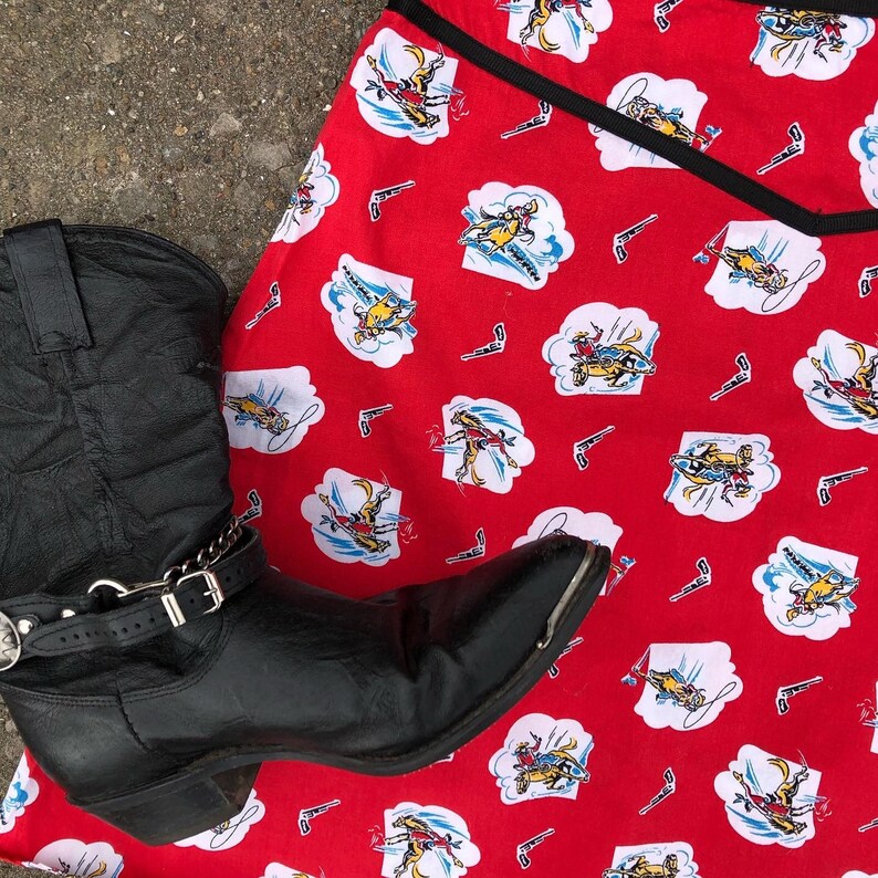 Peut inclure: Une botte de cowboy en cuir noir avec des boucles argent&eacute;es et une jupe en tissu rouge et blanc avec un motif de cowboy.