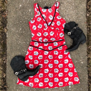 Peut inclure: Une robe rouge sans manches avec une bordure noire et un motif blanc et rouge de cowboys &agrave; cheval. La robe est associ&eacute;e &agrave; deux bottes de cowboy noires.