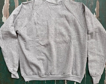 May include: A heather gray sweatshirt with a mock neck collar and long sleeves. The cuffs and hem are ribbed. The raglan sleeves extend from the collar to the underarm. The fabric has a textured appearance.