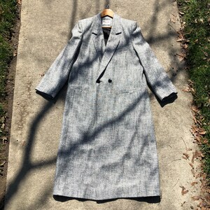 May include: A long, gray tweed coat with a double-breasted closure and a notched collar.