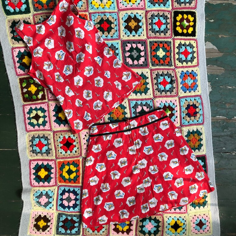 Peut inclure: Un ensemble jupe et haut &agrave; motifs rouge et blanc. La jupe a une ceinture noire et le haut a un col rond. L'ensemble est dispos&eacute; sur une couverture en crochet color&eacute;e.