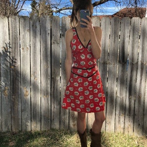 Peut inclure: Une robe rouge sans manches avec un imprim&eacute; floral blanc et une bordure noire. La robe a un d&eacute;collet&eacute; en V et un corsage ajust&eacute;. La jupe est &eacute;vas&eacute;e et arrive juste au-dessus des genoux.