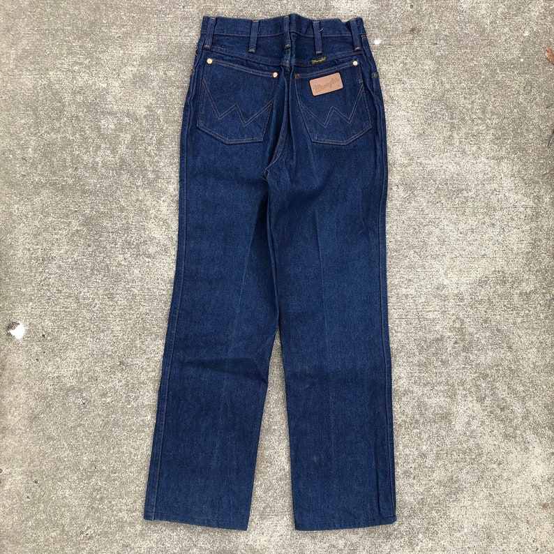 May include: A pair of dark blue denim jeans with a brown leather patch on the back pocket that says "Wrangler".