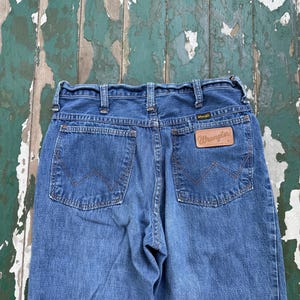 Op de afbeelding: Blauwe Wrangler-jeans van denim met een klassiek ontwerp met vijf zakken. De jeans hebben een bruine leren patch met het Wrangler-logo op de achterzak. De jeans hebben een medium wassing en een rechte pijp.