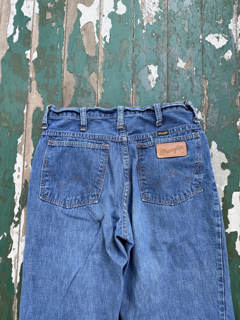 Op de afbeelding: Blauwe Wrangler-jeans van denim met een klassiek ontwerp met vijf zakken. De jeans hebben een bruine leren patch met het Wrangler-logo op de achterzak. De jeans hebben een medium wassing en een rechte pijp.