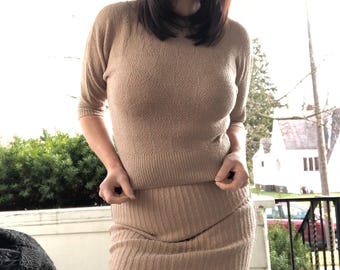 May include: A beige knitted sweater and skirt set. The sweater has a round neckline and three-quarter sleeves. The skirt is a pencil skirt.