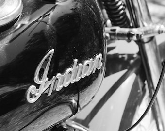 May include: Black and white photo of a motorcycle gas tank with a chrome "Indian" logo.