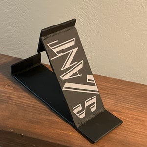 Könnte beinhalten: Ein schwarzer Telefonständer aus Metall mit einem weißen grafischen Design, auf dem vorne "INZA" steht.