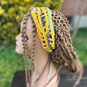 May include: A colorful crochet headband in yellow, green, blue, and orange. The headband is worn on a mannequin head with long, brown, curly hair. The crochet design features an open, woven pattern.