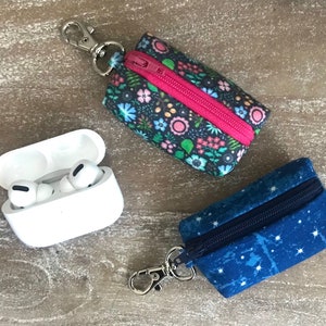 May include: Two zippered pouches with keychains, one with a floral print and the other with a blue starry print. A white case with two white earbuds inside.