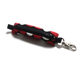 May include: A red and black polka dot zippered pouch with a silver key ring. The pouch is about 4 inches long.