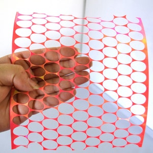 May include: A flexible, rectangular sheet featuring a repeating grid pattern of circular cutouts. The material has a vibrant, iridescent orange and pink finish that shifts in color, creating a semi-transparent effect across the surface.