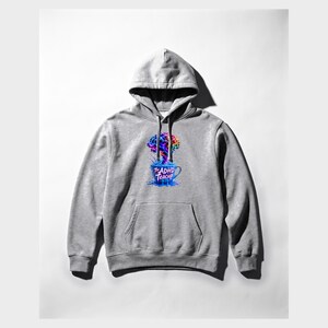 Peut inclure: Un sweat-shirt &agrave; capuche gris clair avec une impression graphique sur la poitrine. Le motif repr&eacute;sente une tasse &agrave; th&eacute; bleue d&eacute;bordant d'une explosion de peinture color&eacute;e en forme de cerveau. Le texte "The ADHD Teacup" est imprim&eacute; en rose.