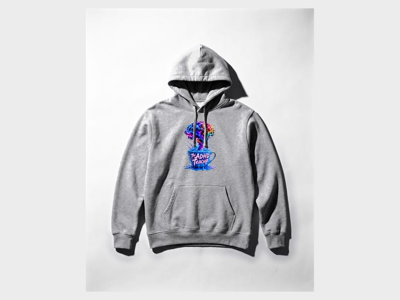 Peut inclure: Un sweat-shirt &agrave; capuche gris clair avec une impression graphique sur la poitrine. Le motif repr&eacute;sente une tasse &agrave; th&eacute; bleue d&eacute;bordant d'une explosion de peinture color&eacute;e en forme de cerveau. Le texte "The ADHD Teacup" est imprim&eacute; en rose.