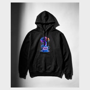 Peut inclure: Un sweat-shirt &agrave; capuche noir avec une impression graphique sur la poitrine. Le motif repr&eacute;sente un cerveau color&eacute; aux teintes multiples s'&eacute;levant comme de la vapeur d'une tasse bleue. Le texte sur la tasse indique The ADHD Teacup.