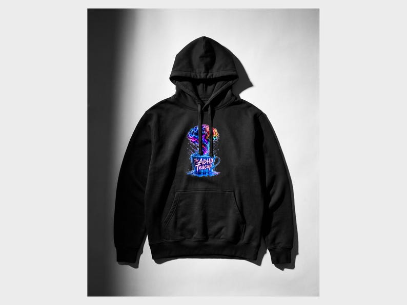 Peut inclure: Un sweat-shirt &agrave; capuche noir avec une impression graphique sur la poitrine. Le motif repr&eacute;sente un cerveau color&eacute; aux teintes multiples s'&eacute;levant comme de la vapeur d'une tasse bleue. Le texte sur la tasse indique The ADHD Teacup.