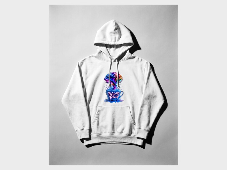 Peut inclure: Un sweat-shirt &agrave; capuche blanc avec une impression graphique sur la poitrine. Le motif repr&eacute;sente une tasse &agrave; th&eacute; bleue d&eacute;bordant d'un nuage de fum&eacute;e color&eacute; en forme de cerveau et le texte The ADHD Teacup en police rose et bleue.