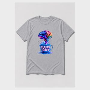 Puede incluir: Una camiseta gris jaspeado de manga corta con un gr&aacute;fico de una taza de t&eacute; azul de la que sale una nube arremolinada, multicolor y con forma de cerebro. El texto "The ADHD Teacup" est&aacute; impreso en blanco en la parte frontal de la taza.