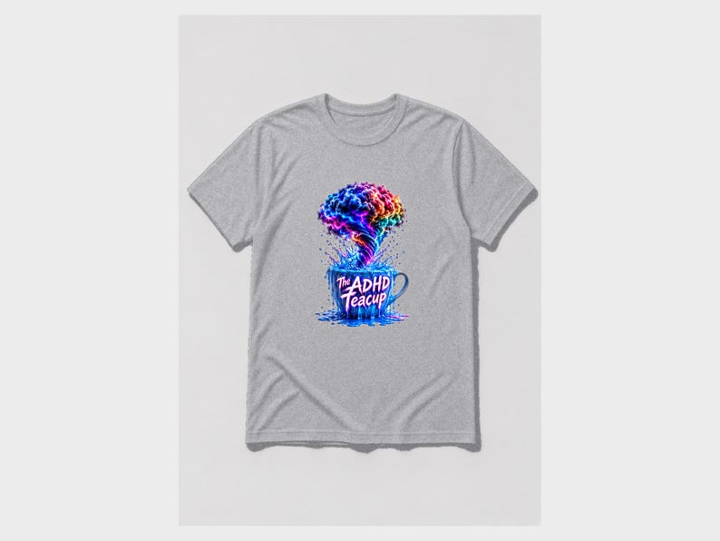 Puede incluir: Una camiseta gris jaspeado de manga corta con un gr&aacute;fico de una taza de t&eacute; azul de la que sale una nube arremolinada, multicolor y con forma de cerebro. El texto "The ADHD Teacup" est&aacute; impreso en blanco en la parte frontal de la taza.