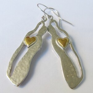 May include: Silver dangle earrings with a cutout design and a gold heart accent.