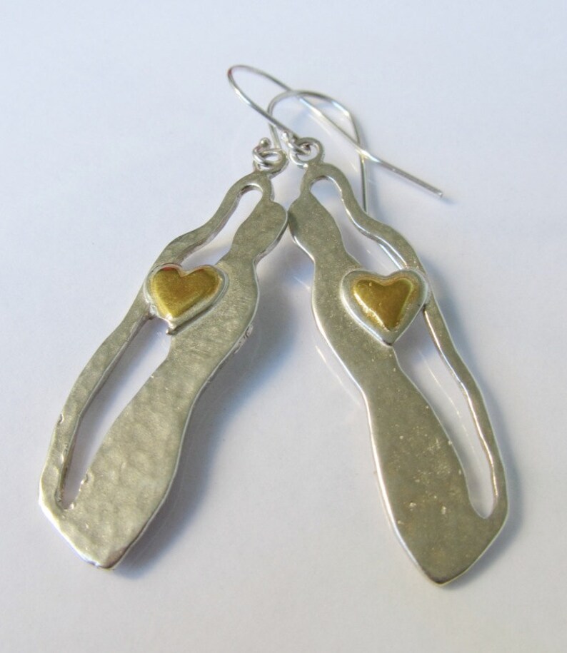 May include: Silver dangle earrings with a cutout design and a gold heart accent.