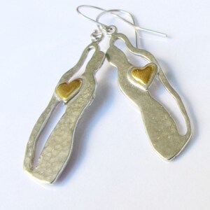 May include: Silver dangle earrings with a cutout design and a gold heart accent.