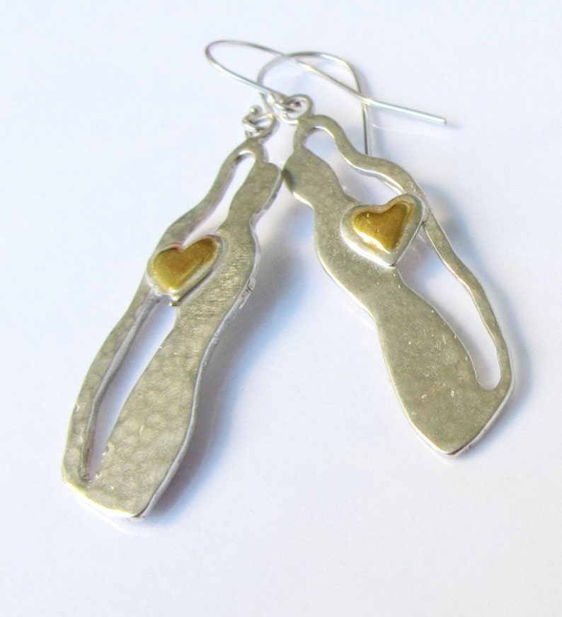 May include: Silver dangle earrings with a cutout design and a gold heart accent.