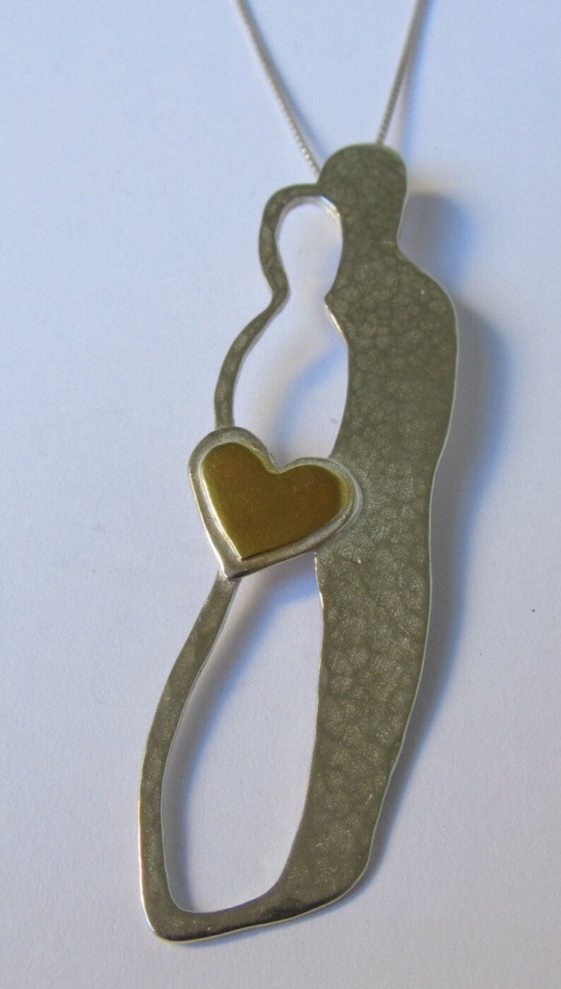 May include: A silver necklace with a pendant shaped like two figures holding a gold heart. The pendant has a textured surface.