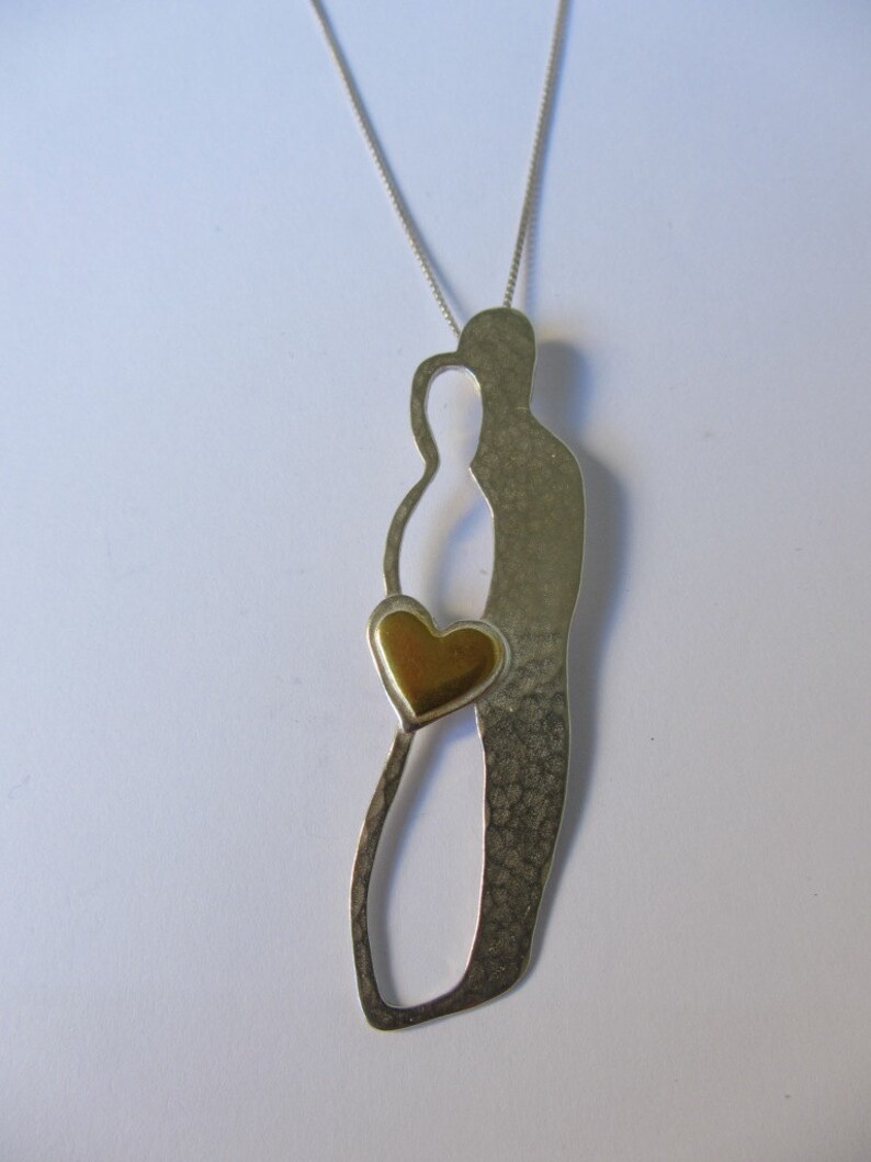 May include: A silver necklace with a pendant featuring two stylised figures holding a gold heart. The pendant has a textured finish.