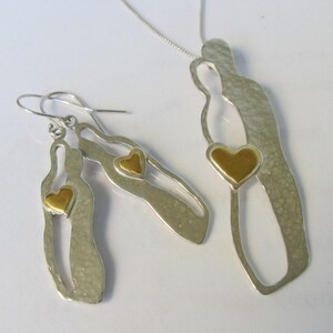 May include: A silver necklace and earrings set featuring two stylised figures with gold hearts. The figures are cut out and have a textured surface.