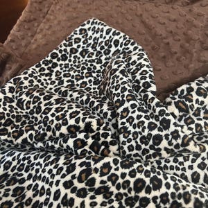 May include: A brown and white leopard print blanket with a brown minky backing. The blanket is folded in half and the leopard print side is facing up.