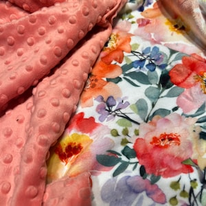 May include: A pink minky fabric with a white background featuring a watercolor floral print. The floral print includes pink, orange, yellow, and purple flowers.