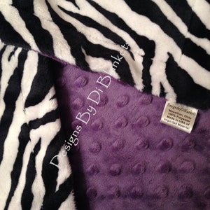 May include: A purple minky baby blanket with a black and white zebra print on one side. The blanket is made of 100% polyester and is made in the USA of imported materials. Designs By Di Blankets.