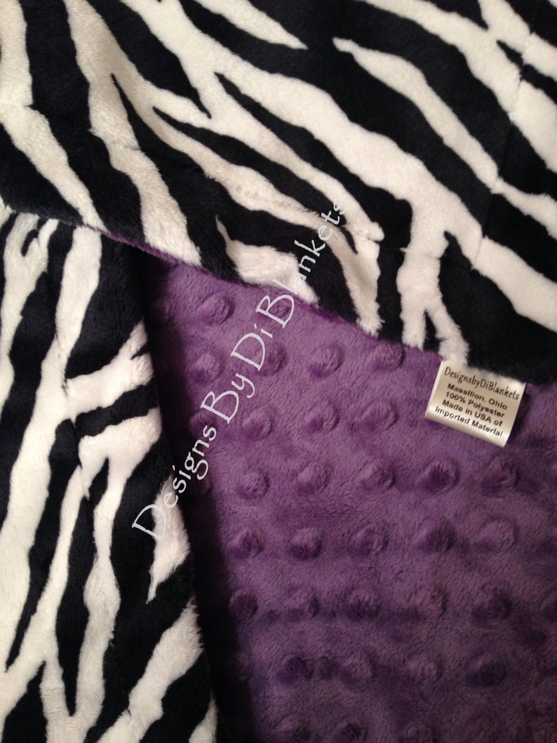 May include: A purple minky baby blanket with a black and white zebra print on one side. The blanket is made of 100% polyester and is made in the USA of imported materials. Designs By Di Blankets.