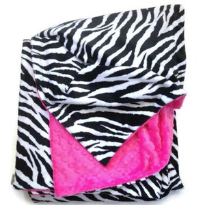 May include: A black and white zebra print blanket with a bright pink fleece lining. The blanket is folded in half and the pink side is facing up.