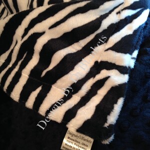 May include: Close-up of a black and white zebra print fabric with a tag that reads "Designsby DiBlankets Massillon, Ohio 100% Polyester Made in USA of Imported Material".
