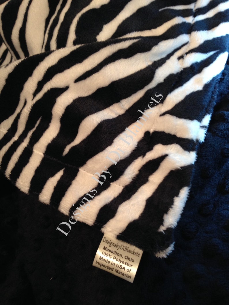 May include: Close-up of a black and white zebra print fabric with a tag that reads "Designsby DiBlankets Massillon, Ohio 100% Polyester Made in USA of Imported Material".