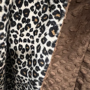 May include: A soft, brown and white blanket with a leopard print on one side and a textured, brown fabric on the other side.