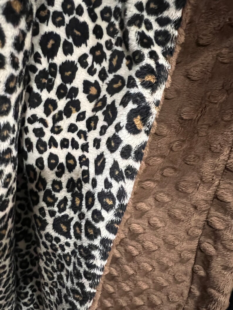 May include: A soft, brown and white blanket with a leopard print on one side and a textured, brown fabric on the other side.