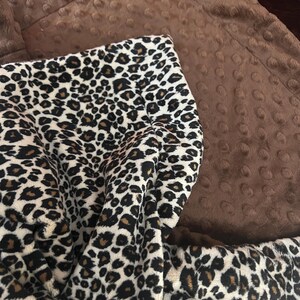 May include: A brown and white leopard print blanket with a brown minky backing. The blanket is soft and cuddly, perfect for snuggling up on the couch.
