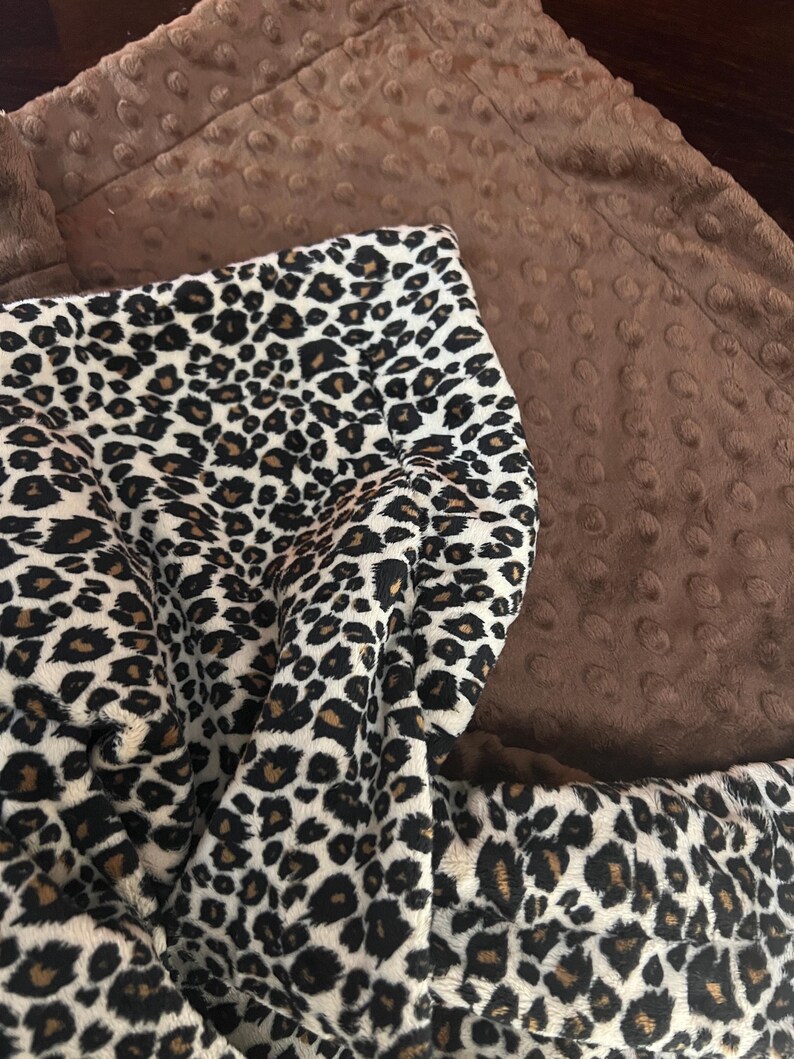 May include: A brown and white leopard print blanket with a brown minky backing. The blanket is soft and cuddly, perfect for snuggling up on the couch.