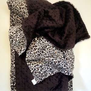 May include: A brown and leopard print fleece blanket. The blanket is folded in half and has a soft, fuzzy texture.